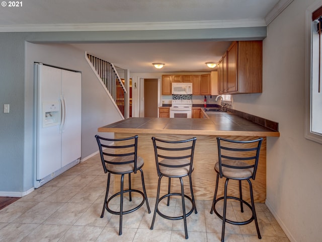 kitchen with white appliances, baseboards, a kitchen breakfast bar, a peninsula, and a sink