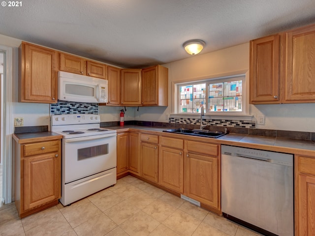 kitchen featuring white appliances, tile counters, a textured ceiling, a sink, and light tile patterned flooring