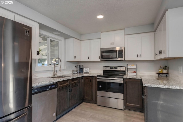 kitchen featuring appliances with stainless steel finishes, light stone counters, sink, light hardwood / wood-style flooring, and white cabinetry