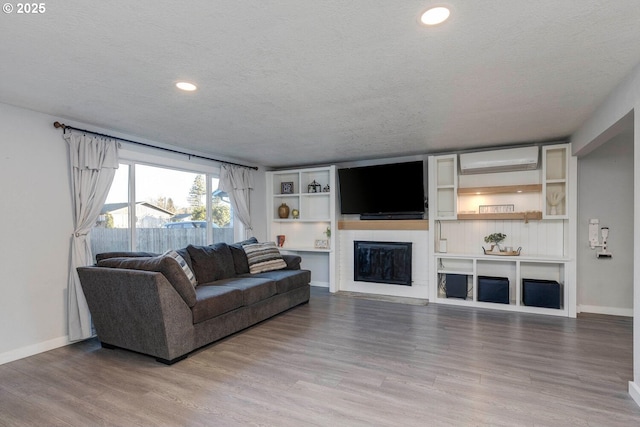 living room with a wall mounted air conditioner, wood-type flooring, and a textured ceiling