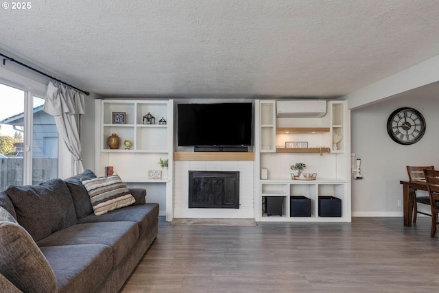 living room featuring a fireplace, a wall mounted air conditioner, hardwood / wood-style floors, and a textured ceiling