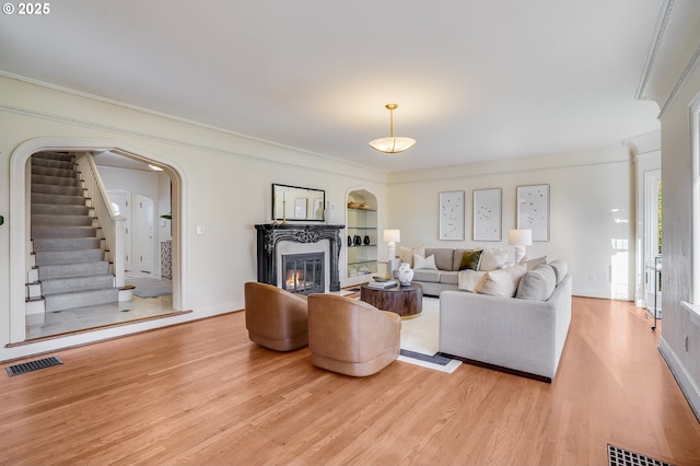2869 SW Champlain Dr, Portland, OR 97205 - living room featuring wood finished floors, ornamental molding, arched walkways, a glass covered fireplace, and stairs