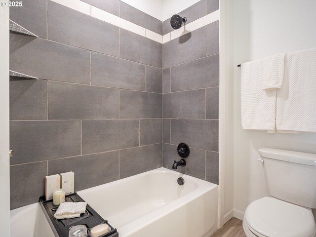 bathroom with tiled shower / bath combo, hardwood / wood-style floors, and toilet