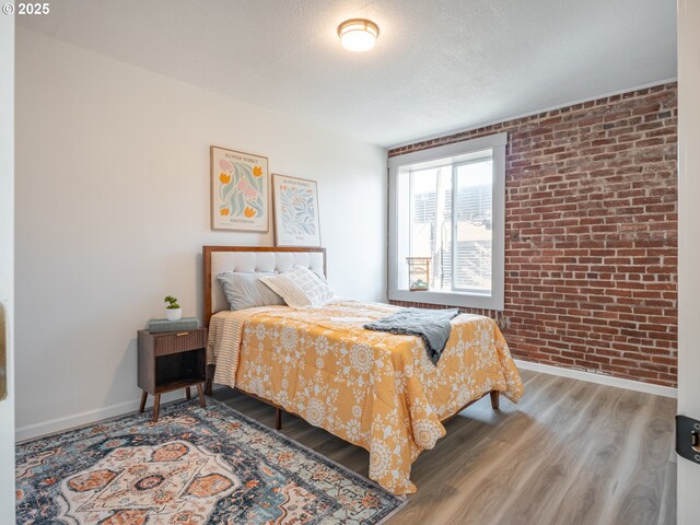 bedroom with hardwood / wood-style flooring, brick wall, and a textured ceiling