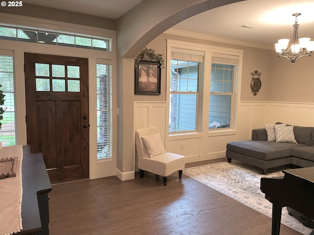 foyer featuring an inviting chandelier, crown molding, visible vents, dark wood-type flooring, and arched walkways