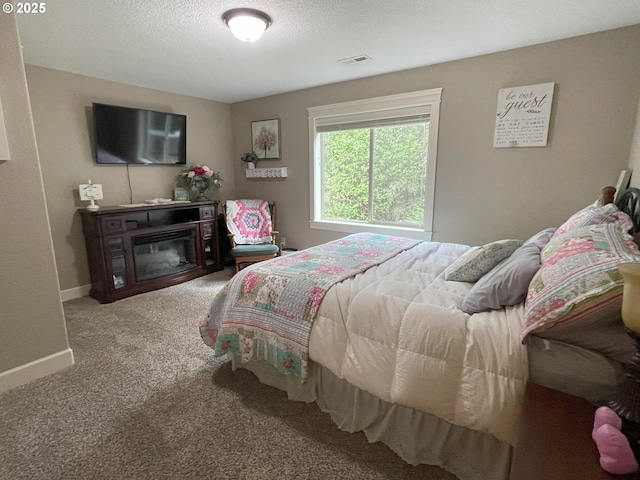 carpeted bedroom featuring baseboards, visible vents, and a glass covered fireplace