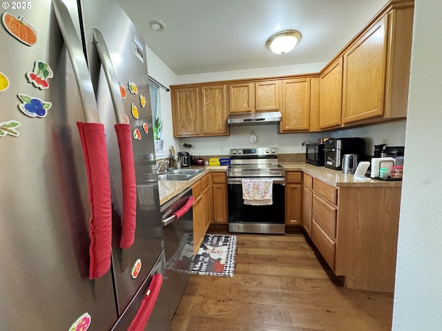 3125 NE Flintlock Pl, Corvallis, OR 97330 - kitchen with appliances with stainless steel finishes, under cabinet range hood, a sink, light wood-style flooring, and light countertops