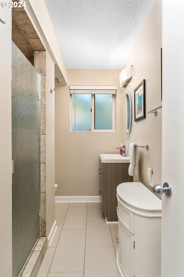 full bath featuring baseboards, tile patterned floors, a textured ceiling, vanity, and a shower stall