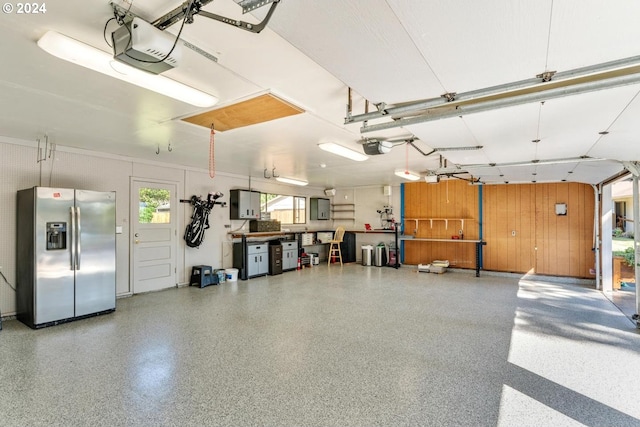 garage with a garage door opener, wooden walls, and stainless steel fridge with ice dispenser