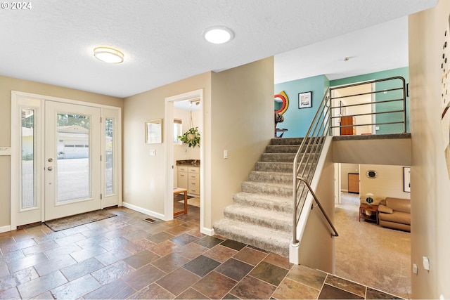 foyer with stairs, a textured ceiling, stone tile flooring, and baseboards