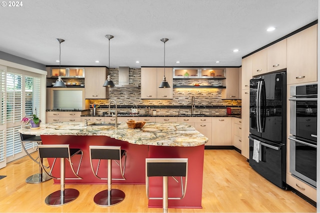 kitchen with light wood-style floors, freestanding refrigerator, stainless steel double oven, a sink, and wall chimney range hood