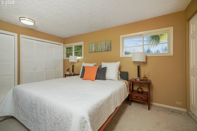 bedroom featuring visible vents, two closets, baseboards, carpet, and a textured ceiling