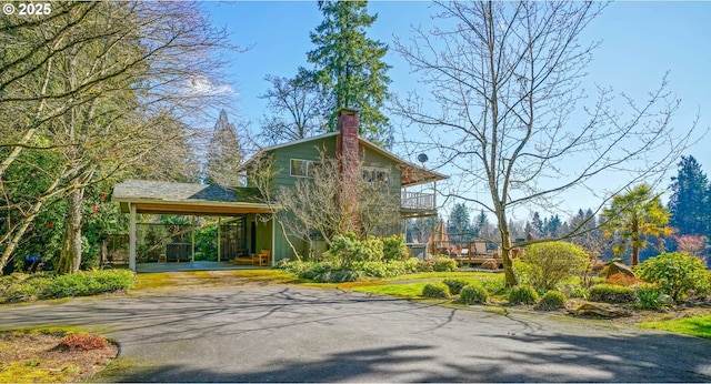 view of front of home with driveway, a chimney, and a balcony