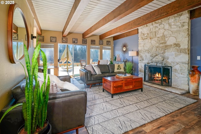 living room featuring beam ceiling, a stone fireplace, and wood finished floors