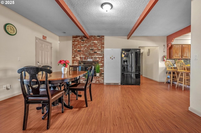 dining space with a brick fireplace, light hardwood / wood-style flooring, beamed ceiling, and a textured ceiling