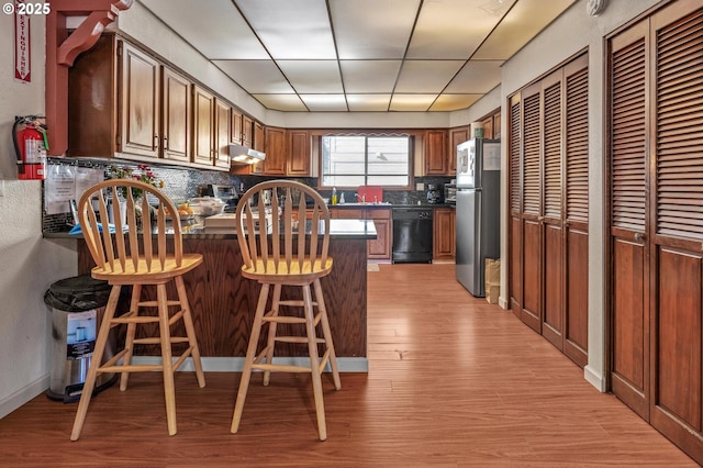 kitchen with stainless steel refrigerator, dishwasher, a kitchen breakfast bar, and decorative backsplash