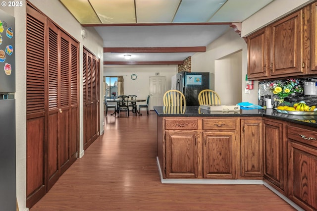 kitchen with black refrigerator, light hardwood / wood-style floors, backsplash, beamed ceiling, and kitchen peninsula