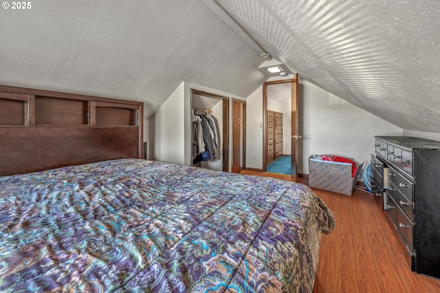 bedroom featuring hardwood / wood-style flooring, a closet, a textured ceiling, vaulted ceiling, and a walk in closet