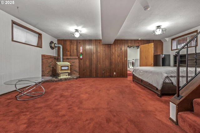 carpeted bedroom featuring a wood stove, washer and dryer, wooden walls, and a textured ceiling