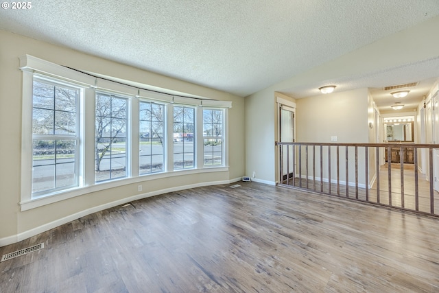 spare room with lofted ceiling, wood finished floors, visible vents, and baseboards