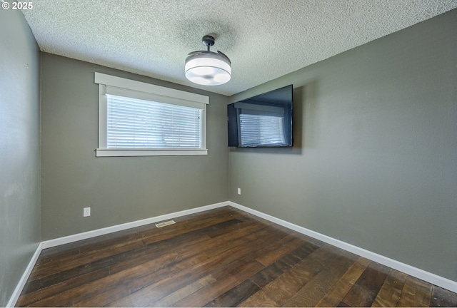 spare room with dark wood-type flooring, visible vents, baseboards, and a textured ceiling