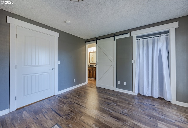 unfurnished bedroom with a barn door, baseboards, dark wood-type flooring, and a textured ceiling