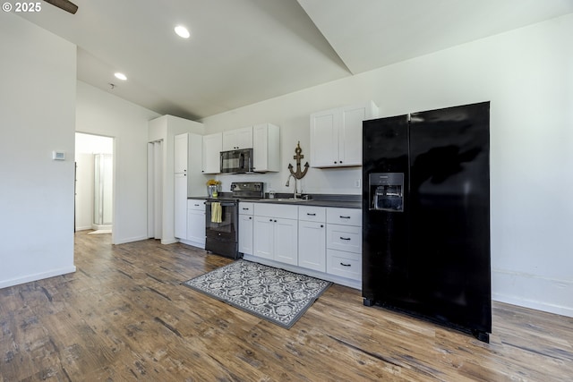 kitchen featuring dark wood-style floors, lofted ceiling, a sink, black appliances, and dark countertops