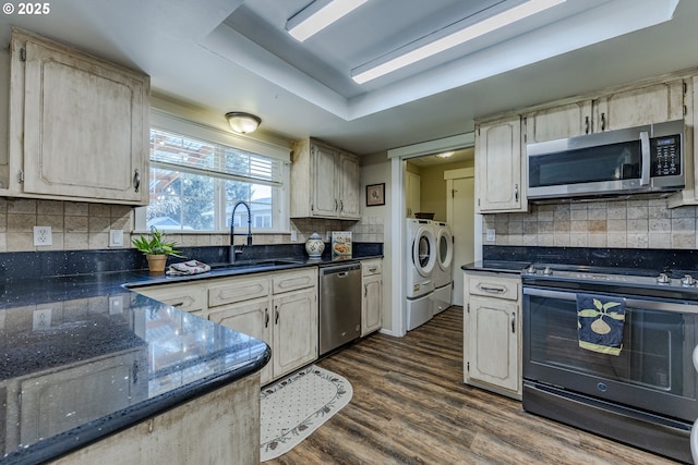 kitchen with washer and clothes dryer, a sink, dark wood finished floors, stainless steel appliances, and a raised ceiling