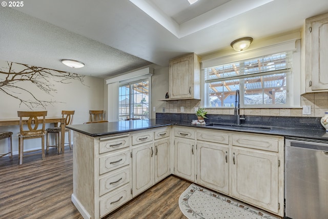 kitchen featuring a sink, tasteful backsplash, stainless steel dishwasher, dark countertops, and dark wood finished floors