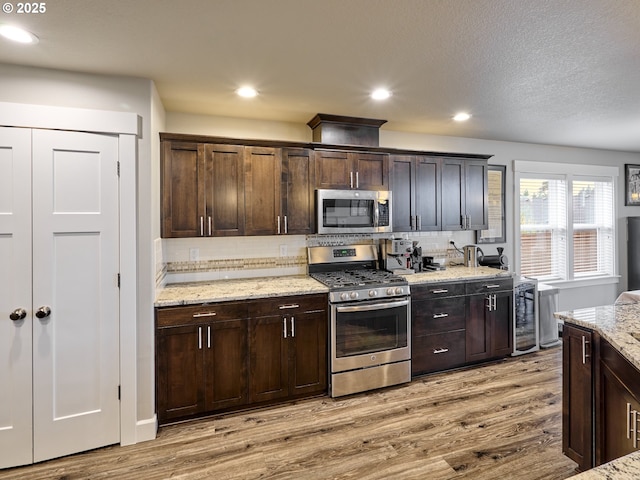 kitchen with light stone countertops, light wood-type flooring, dark brown cabinets, appliances with stainless steel finishes, and tasteful backsplash