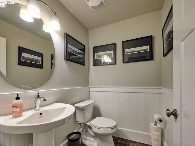 bathroom featuring a wainscoted wall, toilet, a sink, a textured ceiling, and wood finished floors