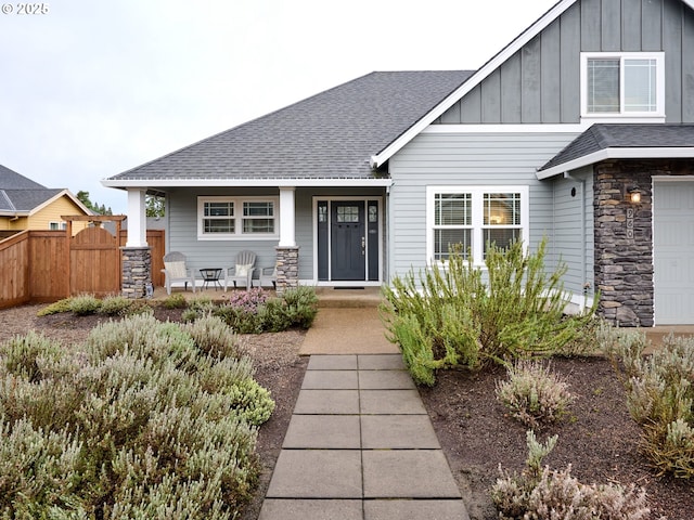 craftsman house with fence, roof with shingles, stone siding, a garage, and board and batten siding