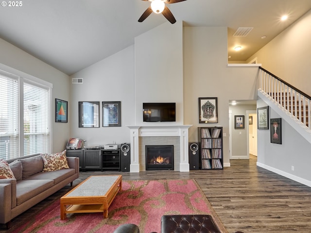 living room featuring a tiled fireplace, wood finished floors, visible vents, and high vaulted ceiling