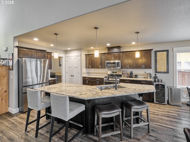 kitchen featuring dark wood finished floors, dark brown cabinets, a kitchen island with sink, and appliances with stainless steel finishes