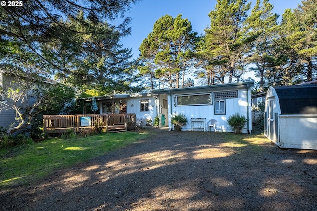 rear view of property with a storage unit, a deck, a lawn, and an outdoor structure