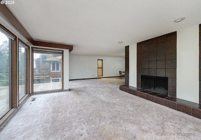 unfurnished living room with a textured ceiling, a tile fireplace, carpet floors, visible vents, and baseboards