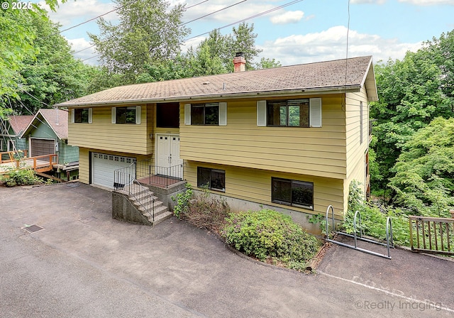 bi-level home with a shingled roof, aphalt driveway, an attached garage, and a chimney