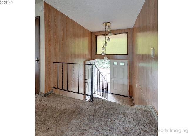 foyer entrance featuring a textured ceiling, light colored carpet, and wooden walls