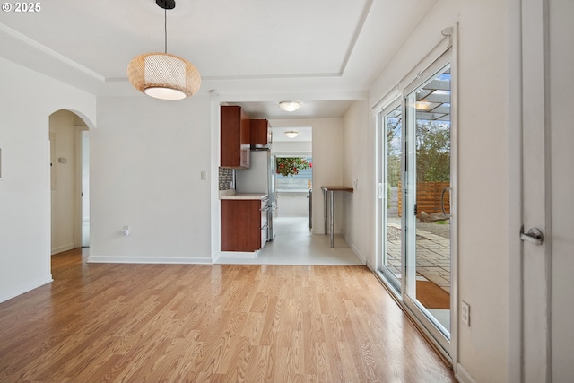 interior space with baseboards, arched walkways, a raised ceiling, and light wood-style floors