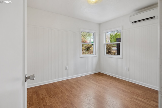 unfurnished room featuring baseboards, wood finished floors, and a wall unit AC