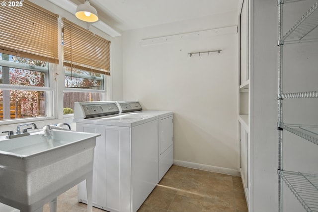 clothes washing area featuring baseboards, a sink, and separate washer and dryer