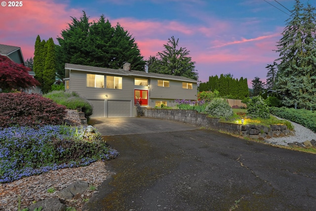 bi-level home featuring asphalt driveway, a chimney, and a garage