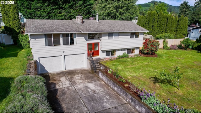 2335 5th St, Columbia City, OR 97018 - split foyer home featuring an attached garage, concrete driveway, a chimney, a view of trees, and roof with shingles