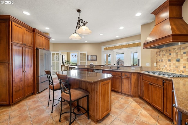 14040 NW Parson Rd, Forest Grove, OR 97116 - kitchen featuring appliances with stainless steel finishes, custom range hood, brown cabinets, a kitchen breakfast bar, and recessed lighting