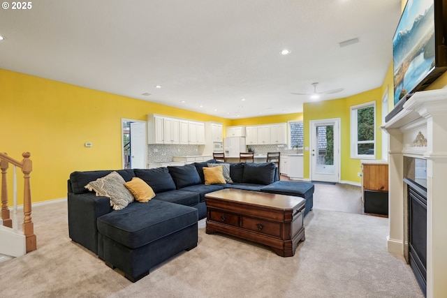 living area with a glass covered fireplace, light carpet, recessed lighting, ceiling fan, and baseboards