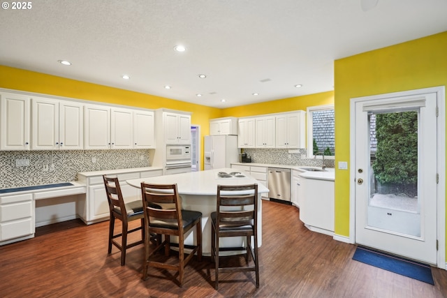 kitchen with a kitchen bar, a sink, a center island, white cabinetry, and white appliances