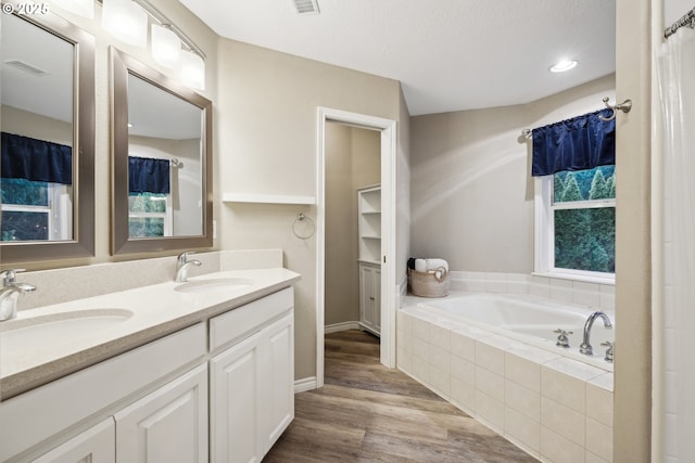 full bath with a bath, double vanity, wood finished floors, healthy amount of natural light, and recessed lighting