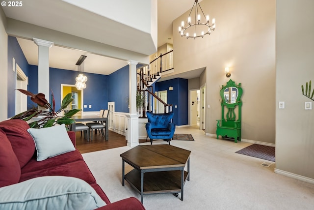 carpeted living room featuring a chandelier, decorative columns, stairway, baseboards, and a towering ceiling
