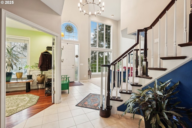 foyer entrance with stairway, baseboards, an inviting chandelier, tile patterned flooring, and a towering ceiling