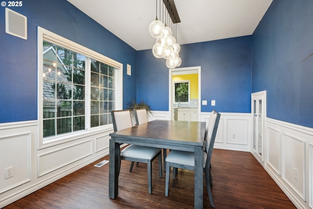 dining space with dark wood-style floors, a decorative wall, a wainscoted wall, and a chandelier